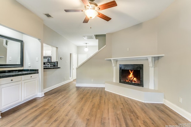 unfurnished living room featuring a tiled fireplace, ceiling fan, and light wood-type flooring