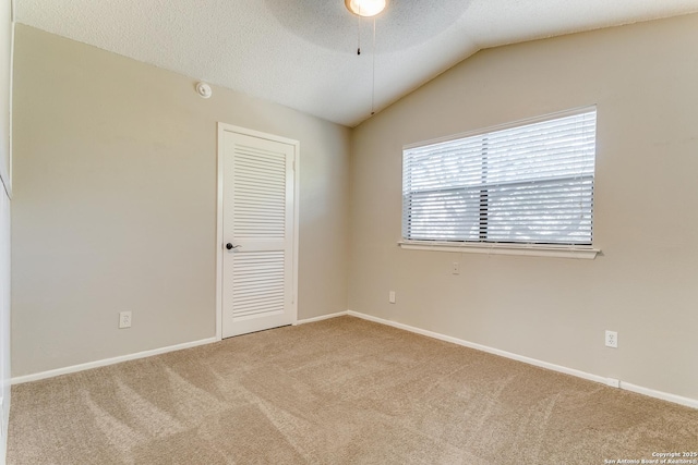 empty room featuring a textured ceiling, ceiling fan, light carpet, and lofted ceiling