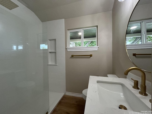 bathroom with a healthy amount of sunlight, wood-type flooring, a tile shower, and toilet