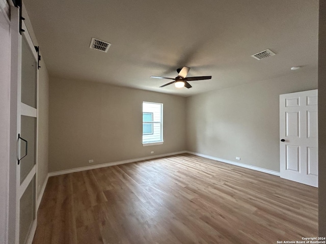 unfurnished room with hardwood / wood-style floors, ceiling fan, and a barn door