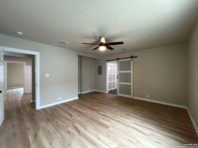 empty room with ceiling fan, light hardwood / wood-style flooring, and a barn door