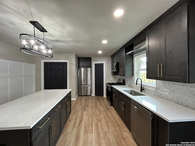 kitchen featuring pendant lighting, stainless steel appliances, tasteful backsplash, light wood-type flooring, and sink