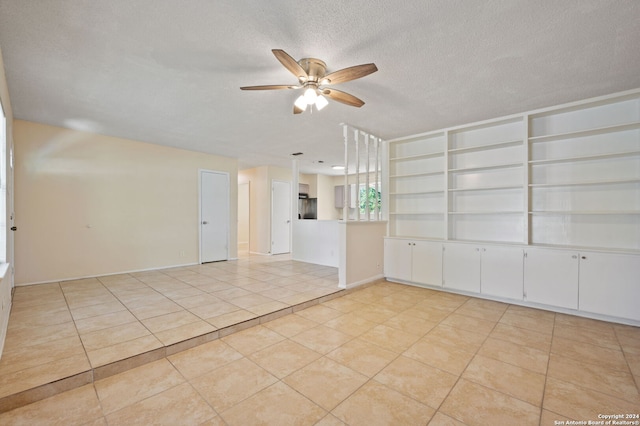 empty room with a textured ceiling, ceiling fan, and light tile patterned flooring