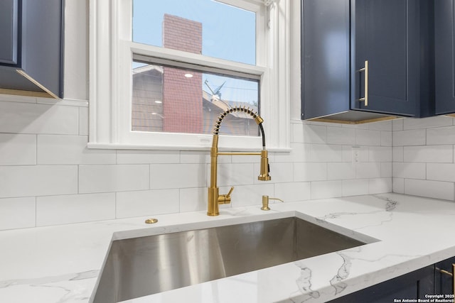 room details featuring tasteful backsplash, light stone countertops, blue cabinetry, and sink