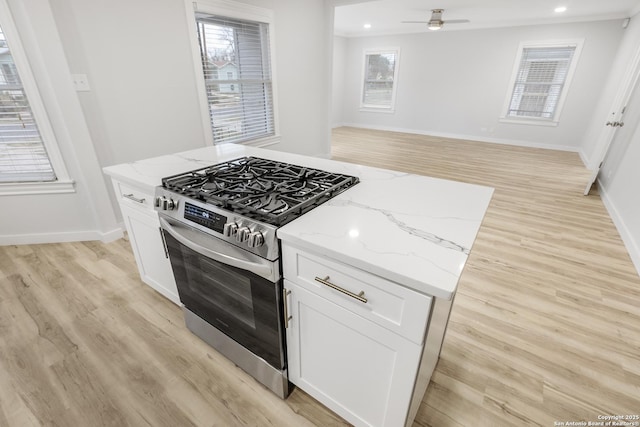 kitchen with light stone countertops, stainless steel gas range, white cabinets, and light hardwood / wood-style flooring