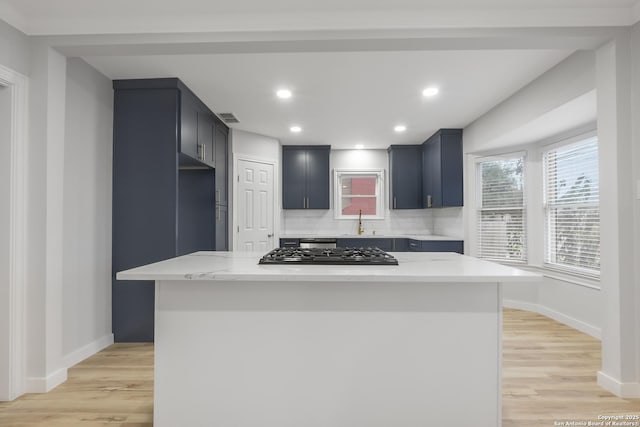 kitchen with sink, a center island, black gas cooktop, decorative backsplash, and light stone countertops