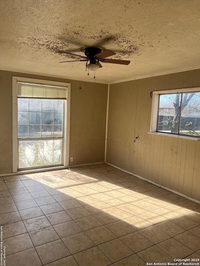 spare room with ceiling fan, wood walls, plenty of natural light, and a textured ceiling