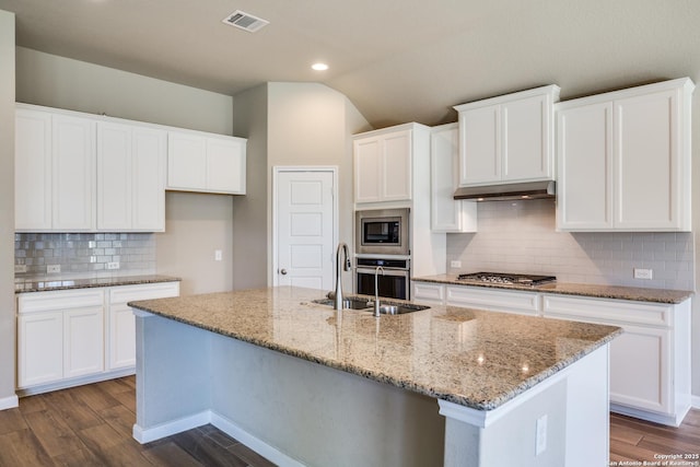 kitchen featuring appliances with stainless steel finishes, an island with sink, light stone counters, white cabinets, and sink