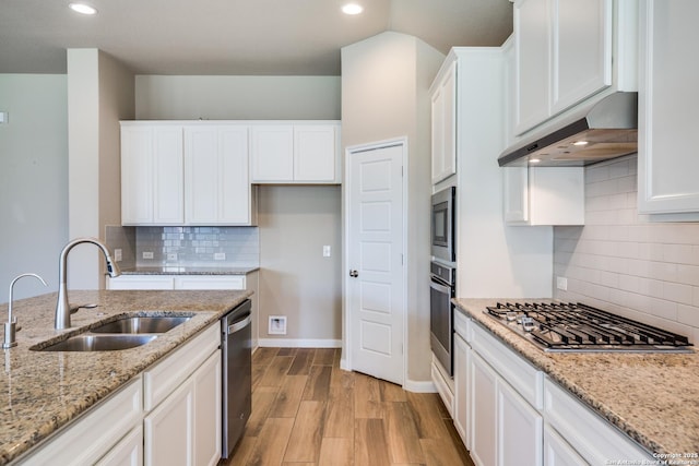 kitchen with appliances with stainless steel finishes, light stone counters, sink, white cabinetry, and range hood