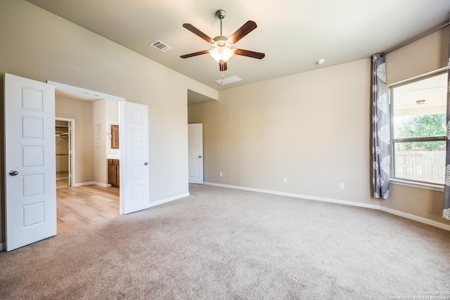 unfurnished bedroom with ceiling fan, light colored carpet, and a walk in closet