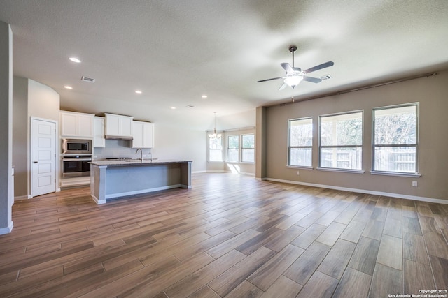 kitchen featuring a kitchen island with sink, stainless steel appliances, ceiling fan, decorative backsplash, and white cabinetry