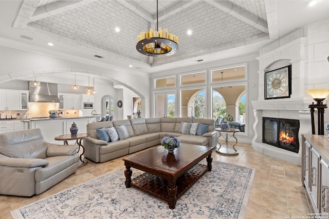 living room with crown molding, a towering ceiling, a large fireplace, a chandelier, and brick ceiling