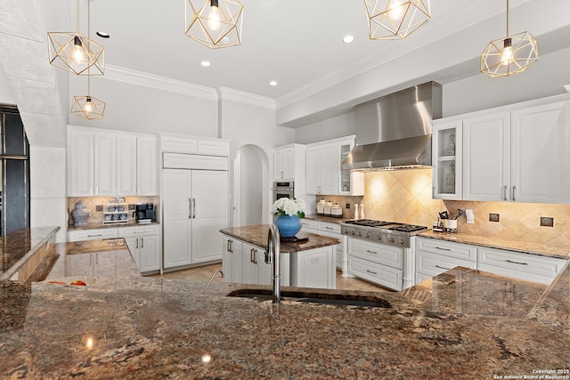 kitchen featuring stainless steel appliances, white cabinetry, hanging light fixtures, and wall chimney exhaust hood