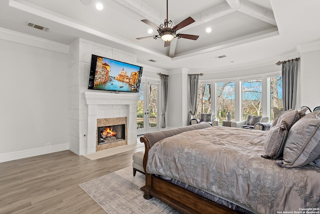 bedroom featuring ceiling fan, hardwood / wood-style floors, ornamental molding, and a large fireplace