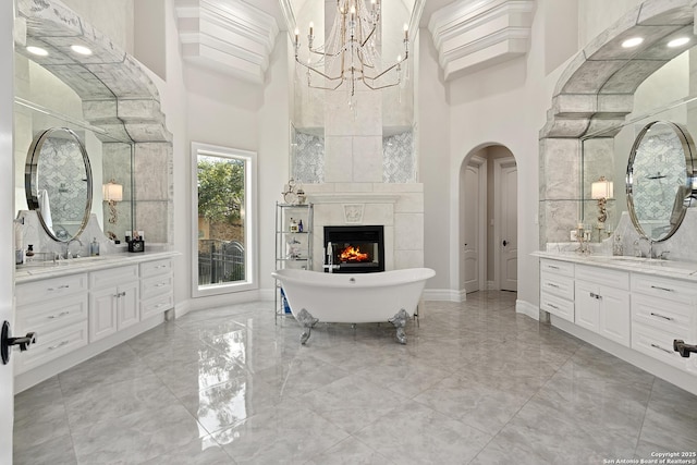 bathroom featuring a towering ceiling, a fireplace, a tub to relax in, and vanity