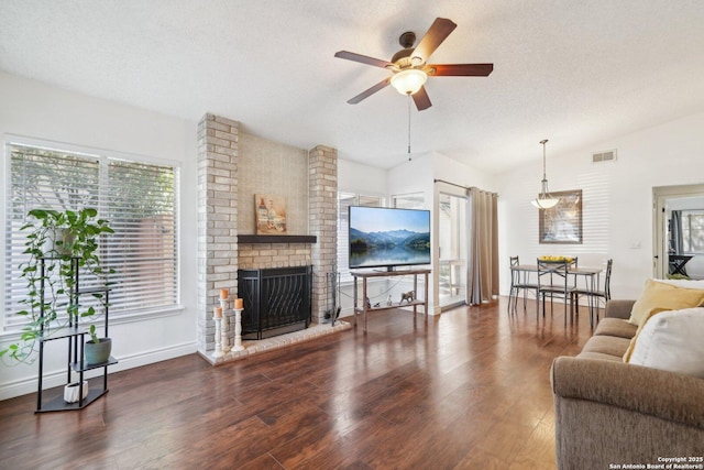 living room featuring vaulted ceiling, ceiling fan, dark wood-type flooring, a brick fireplace, and a textured ceiling