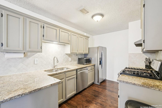 kitchen with sink, stainless steel appliances, a textured ceiling, light stone countertops, and dark wood-type flooring