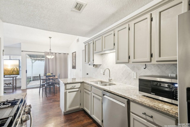 kitchen with appliances with stainless steel finishes, pendant lighting, light stone counters, dark hardwood / wood-style floors, and sink