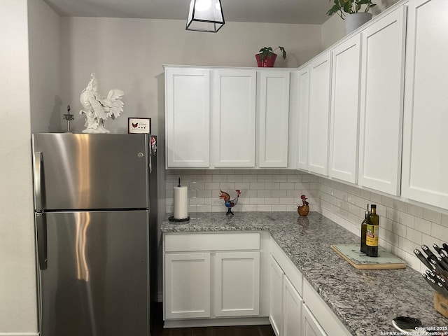 kitchen featuring light stone countertops, stainless steel fridge, backsplash, and white cabinetry