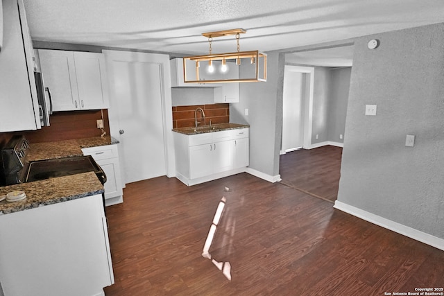 kitchen with hanging light fixtures, electric range, white cabinets, dark stone countertops, and sink