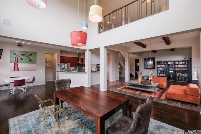 dining space featuring a towering ceiling, dark wood-type flooring, and beam ceiling