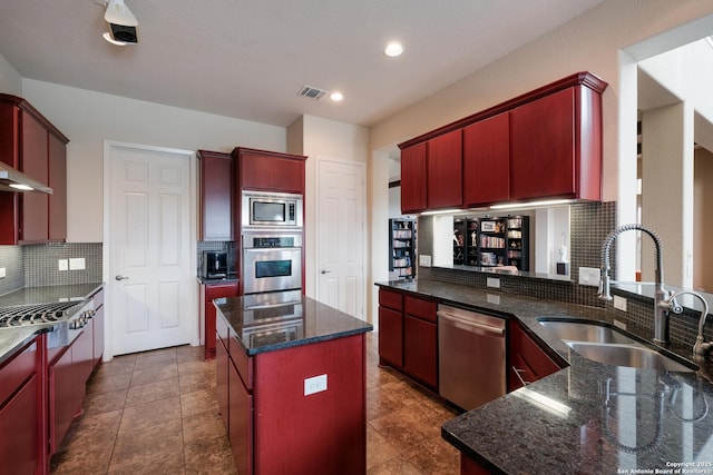 kitchen with stainless steel appliances, sink, a center island, decorative backsplash, and dark stone counters