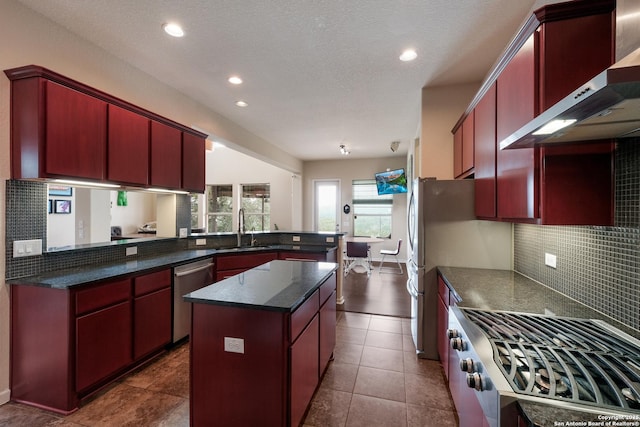 kitchen with sink, stove, kitchen peninsula, stainless steel dishwasher, and wall chimney range hood