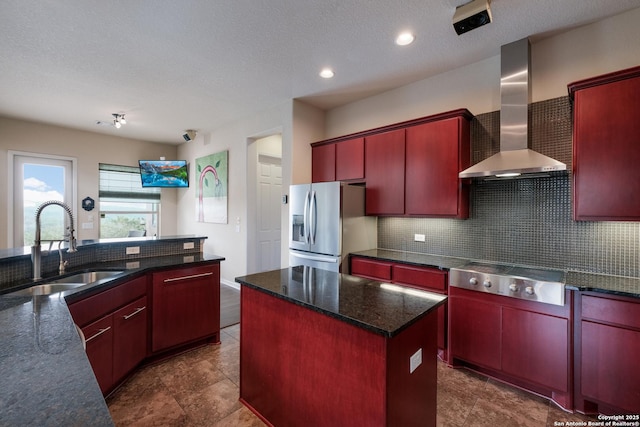 kitchen featuring a textured ceiling, wall chimney exhaust hood, stainless steel appliances, a kitchen island, and sink