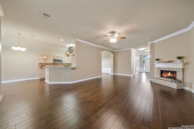 unfurnished living room with dark wood-type flooring, ceiling fan with notable chandelier, crown molding, and a fireplace