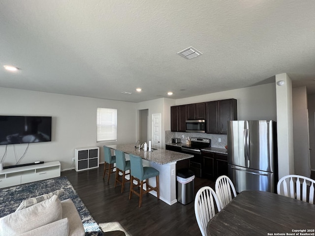 kitchen with a breakfast bar area, a center island with sink, stainless steel appliances, light stone counters, and a textured ceiling