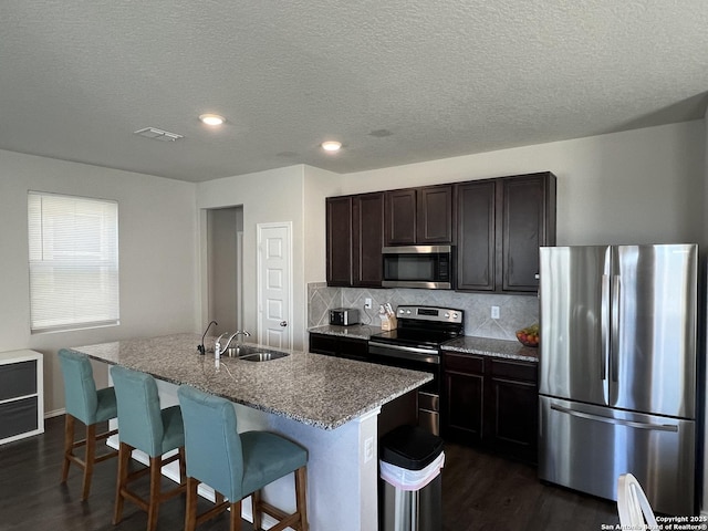 kitchen featuring stainless steel appliances, sink, a kitchen island with sink, dark brown cabinets, and a breakfast bar