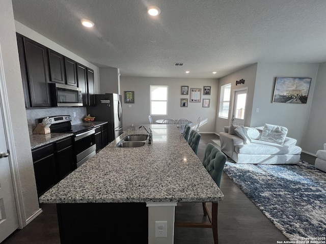 kitchen with stainless steel appliances, sink, a textured ceiling, a kitchen breakfast bar, and a center island with sink