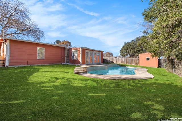 rear view of house featuring french doors, a lawn, a fenced in pool, and a storage shed