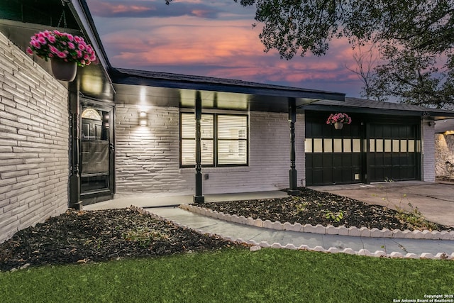 exterior space featuring a garage, concrete driveway, brick siding, and covered porch