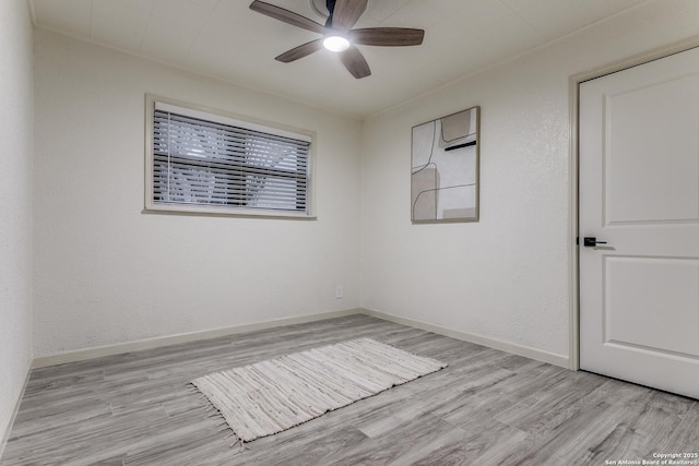 empty room featuring a ceiling fan, a textured wall, light wood-style flooring, and baseboards