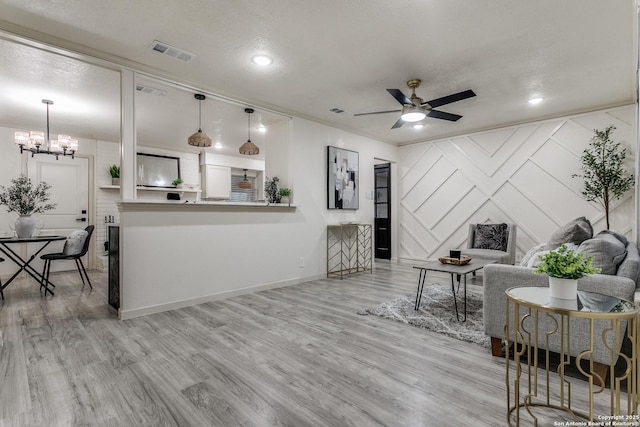 living area with a textured ceiling, visible vents, wood finished floors, and ceiling fan with notable chandelier