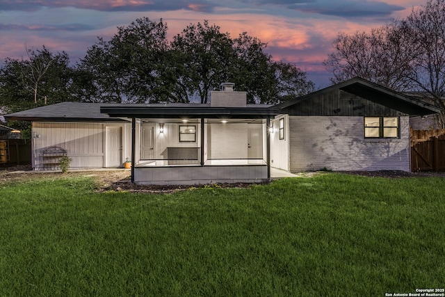 back house at dusk with a lawn and a sunroom