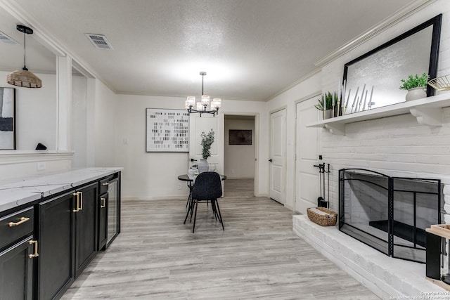 interior space featuring hanging light fixtures, light wood-type flooring, crown molding, light stone counters, and an inviting chandelier