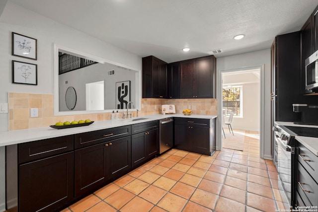 kitchen with a textured ceiling, appliances with stainless steel finishes, backsplash, and light tile patterned floors