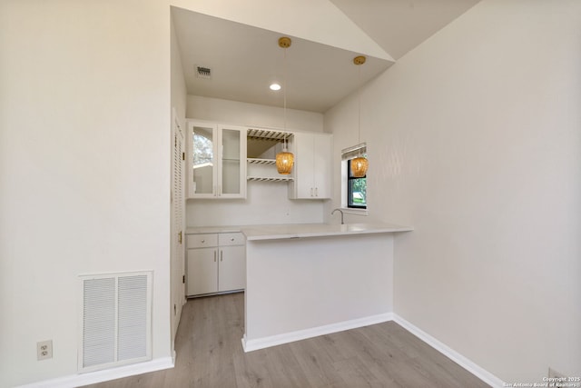 kitchen featuring kitchen peninsula, light wood-type flooring, pendant lighting, and white cabinetry