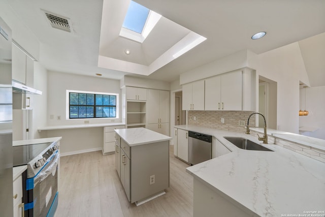 kitchen with a kitchen island, a skylight, white cabinets, appliances with stainless steel finishes, and sink