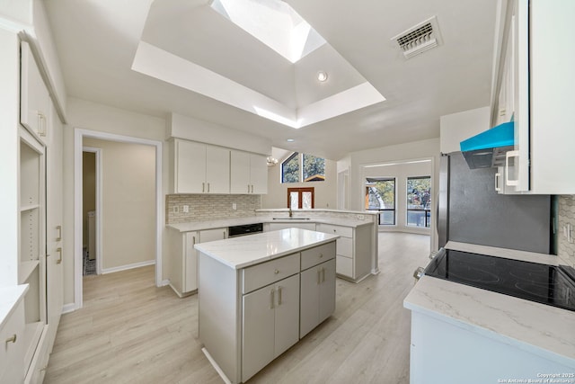 kitchen featuring kitchen peninsula, a raised ceiling, white cabinetry, and a center island