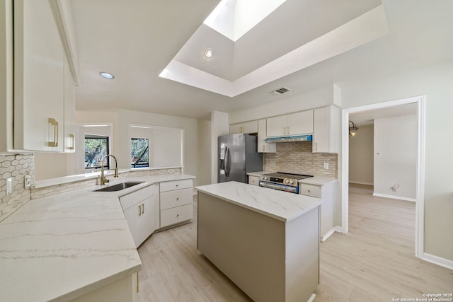 kitchen with light stone counters, stainless steel appliances, a kitchen island, white cabinets, and sink