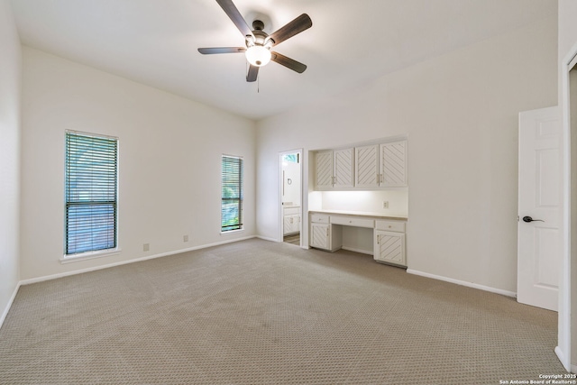 unfurnished bedroom featuring built in desk, ceiling fan, and light colored carpet