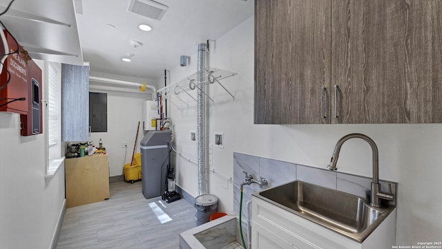 laundry room featuring electric panel, light hardwood / wood-style flooring, water heater, and sink