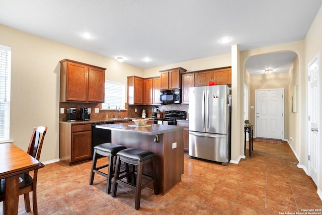 kitchen with black appliances, decorative backsplash, a kitchen island, dark stone countertops, and a kitchen breakfast bar