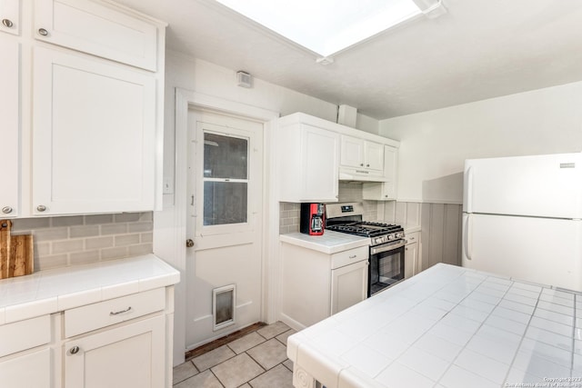 kitchen with white fridge, white cabinetry, gas range, and tile countertops