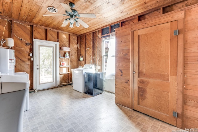 clothes washing area with ceiling fan, water heater, wood walls, washer and dryer, and wood ceiling