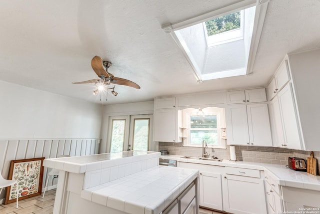 kitchen with white cabinetry, a center island, tile countertops, and a skylight