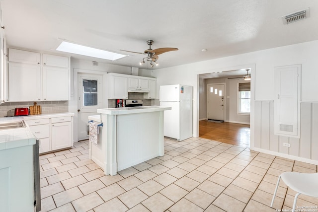 kitchen with backsplash, white refrigerator, a kitchen island, white cabinets, and light tile patterned flooring